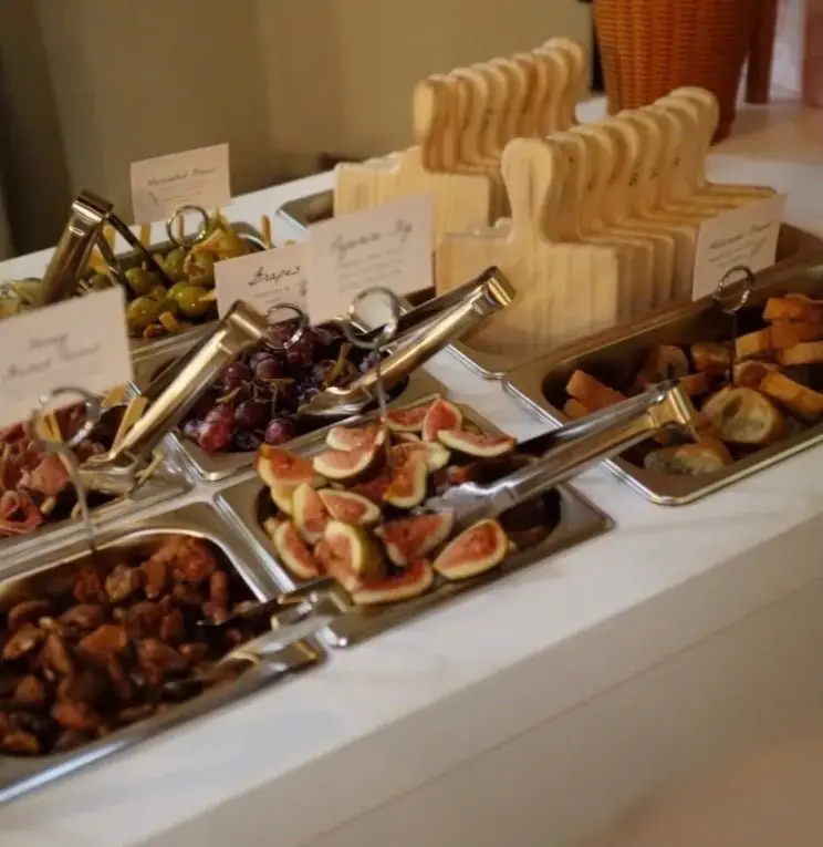 Labelled stainless bins of figs, grapes, olives and candied nuts on the cart, with wooden boards stacked behind